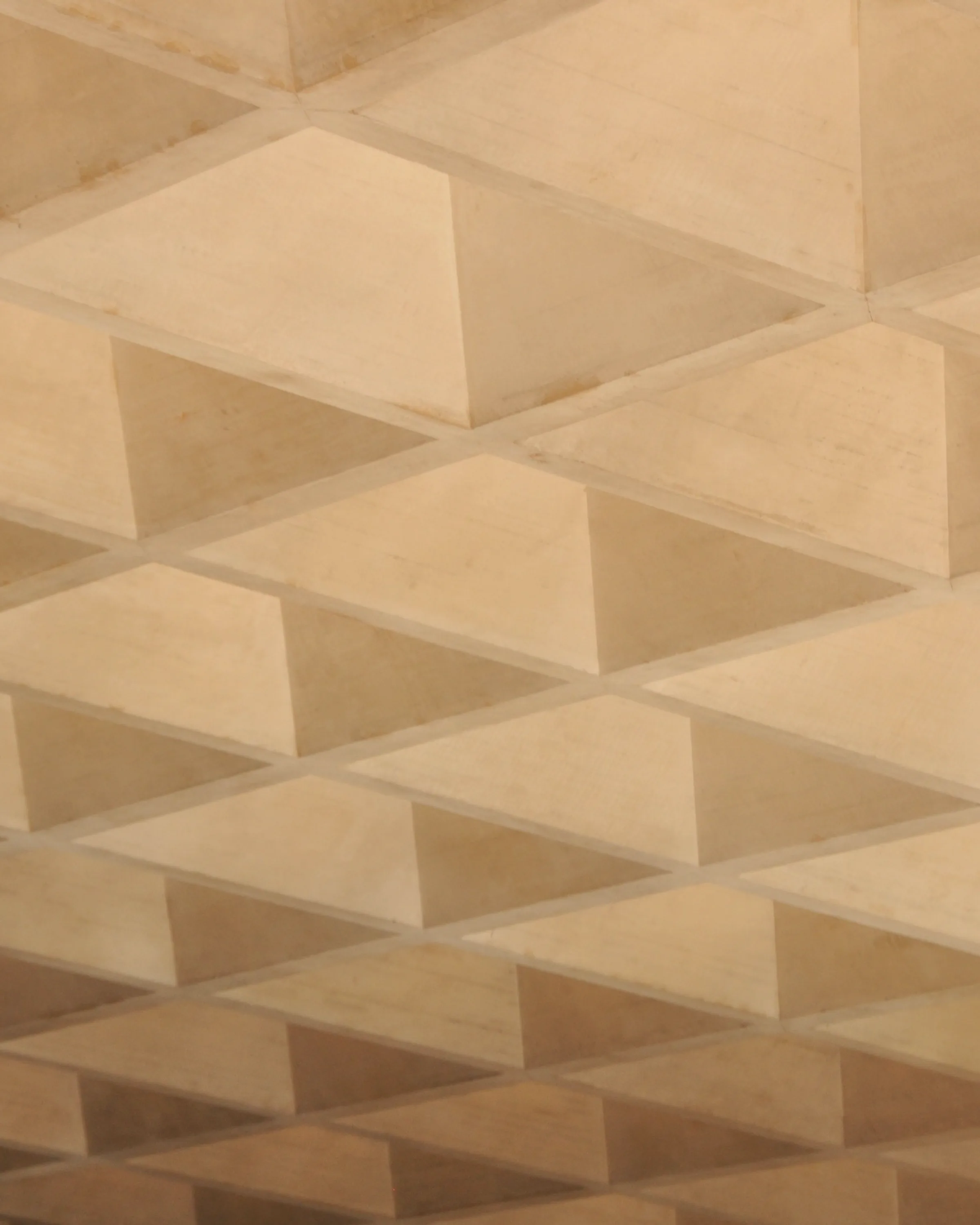 A faceted ceiling in warm metal, its panels folding into shallow pyramids.