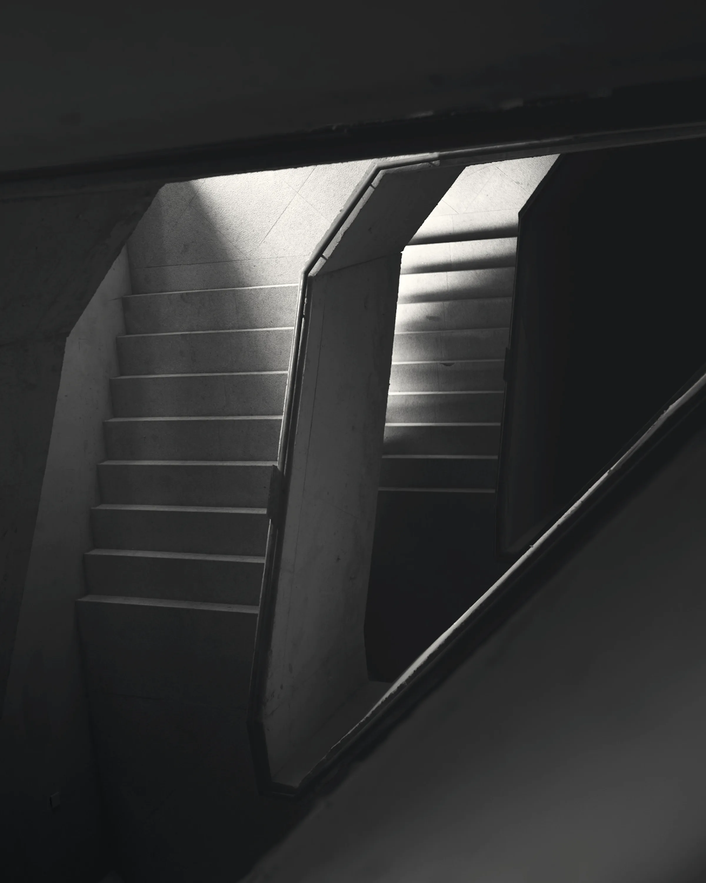 A dark stair crossed by shafts of daylight from openings above.