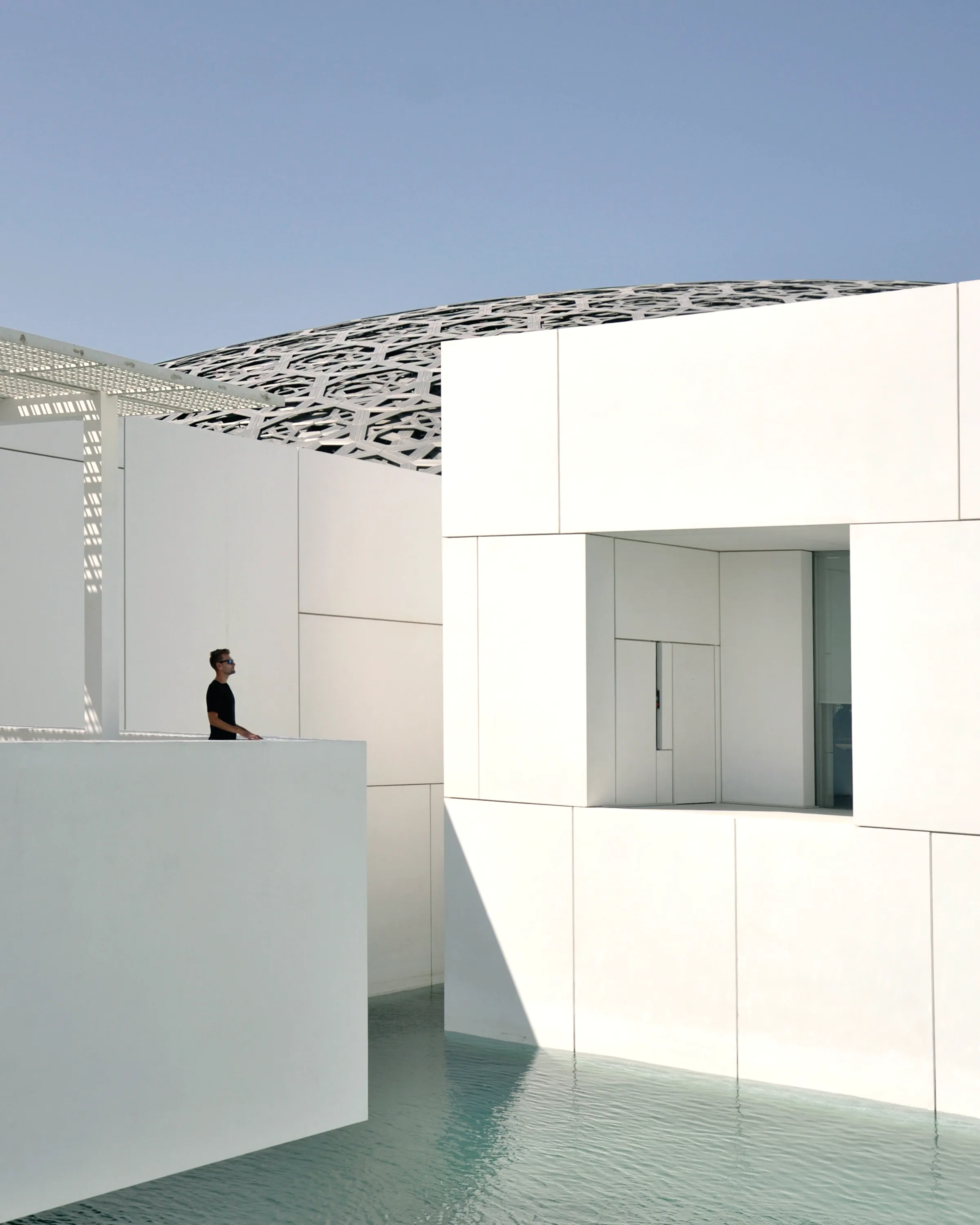 A figure standing in a white gallery interior, the walls meeting without trim.