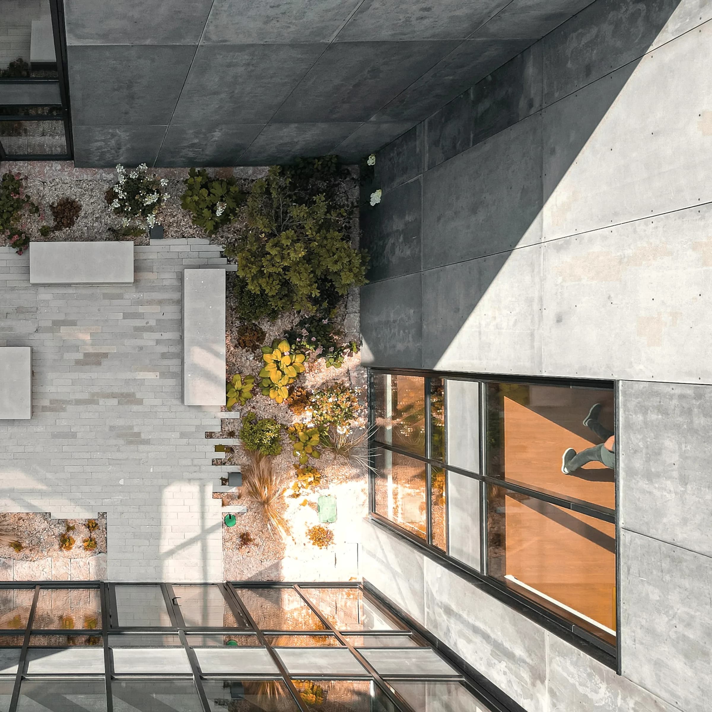 A concrete courtyard seen from directly above, a single stone path crossing it.