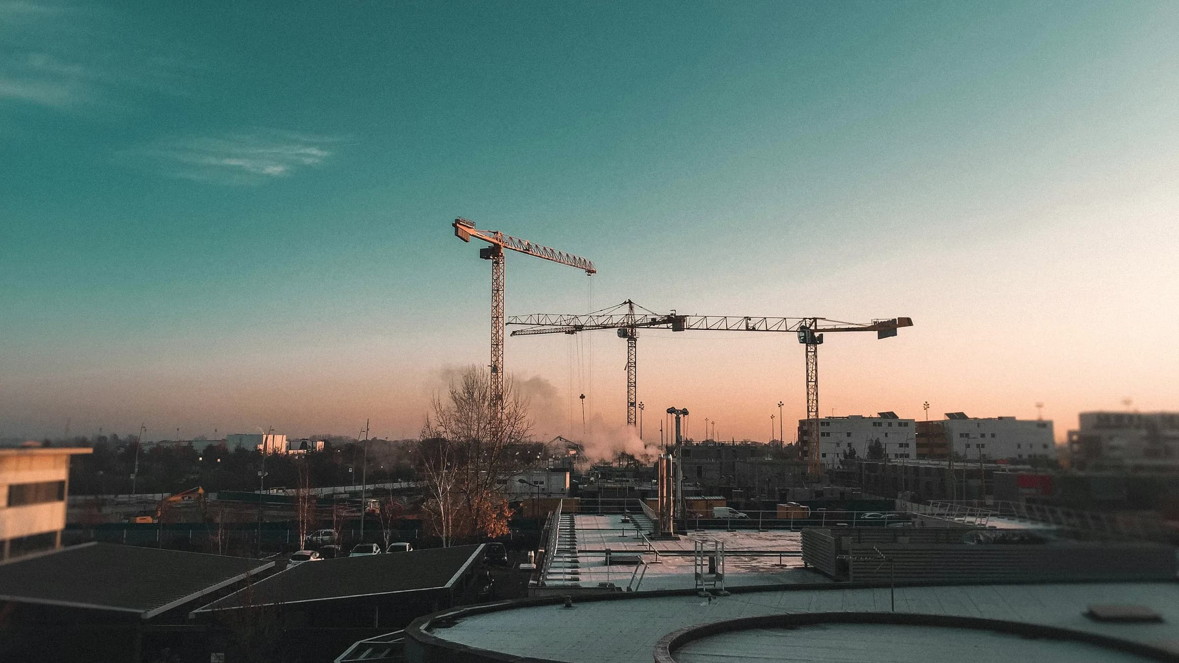 Tower cranes over a construction site in first light.